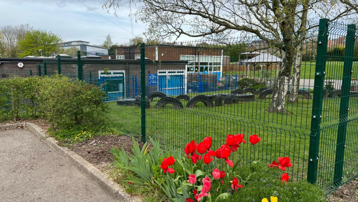 Spring flowers in front of newly installed green security mesh fence around a school playing field