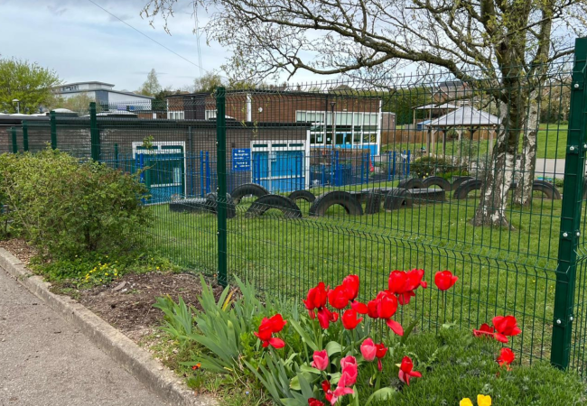 Spring flowers in front of newly installed green security mesh fence around a school playing field